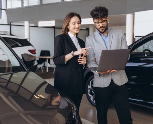 Salespeople at car dealership looking at laptop